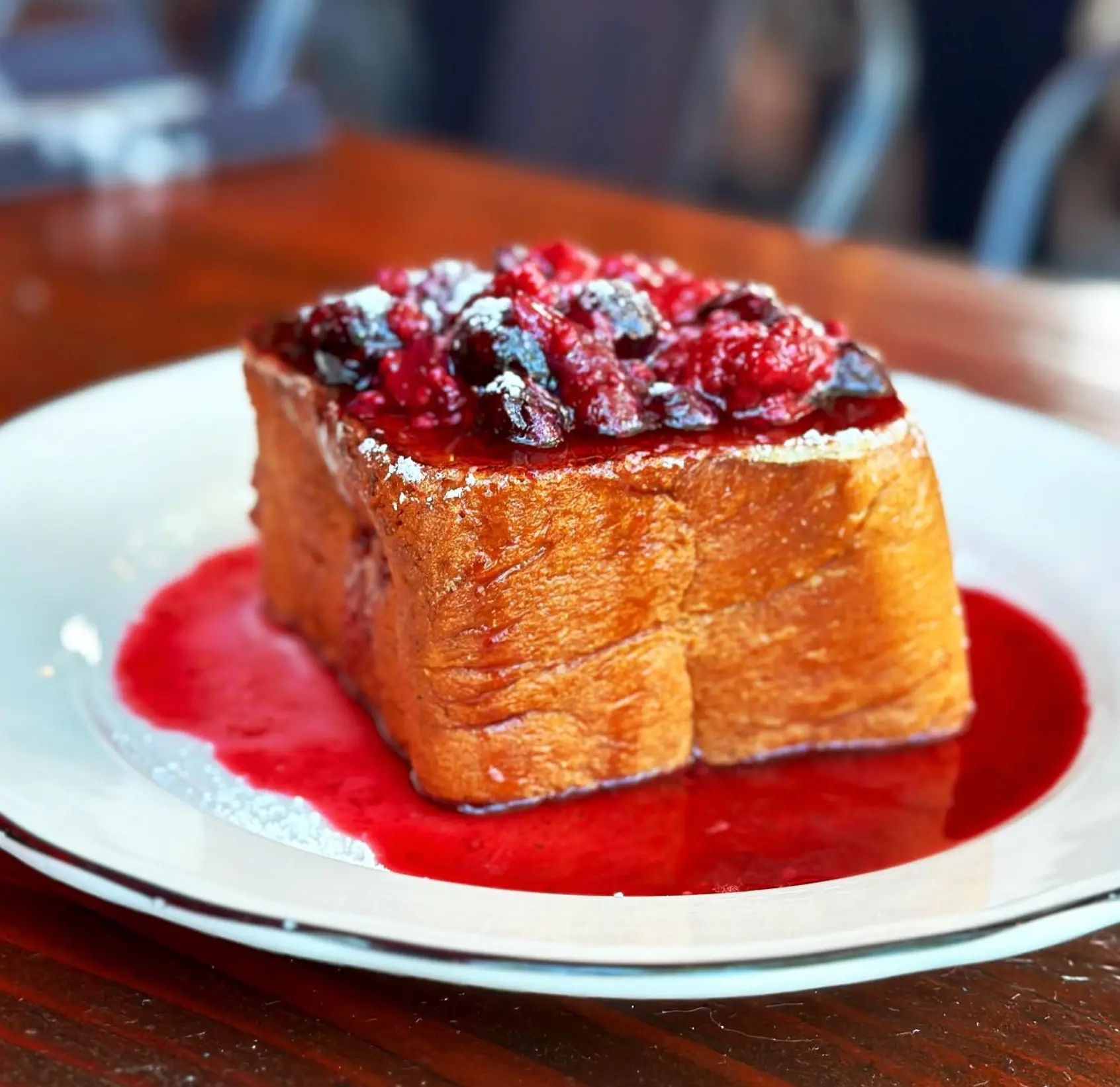 Thick-cut French toast topped with mixed berries and powdered sugar, served in a pool of berry sauce
